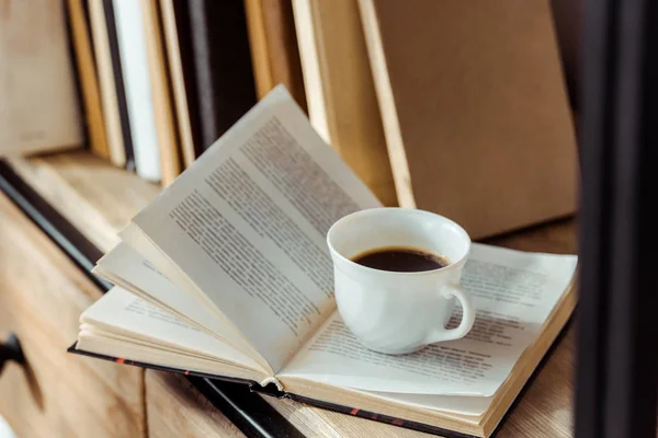 Close up of open book with cup of coffee on bookshelf — Stock Photo