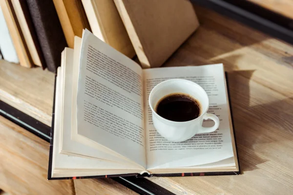 Close up of open book with cup of coffee on bookshelf — Stock Photo