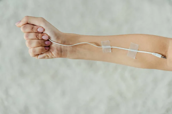 Primer plano de la mano femenina con cable blanco adjunto como infusión IV médica, concepto de música - foto de stock