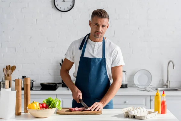 Bell'uomo che taglia carne di maiale in cucina — Foto stock