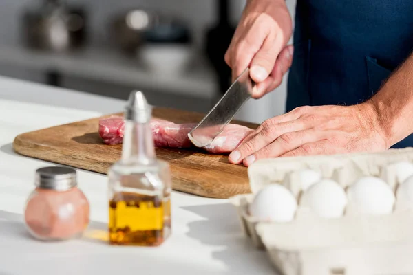 Partial view of man cutting meat on wooden chopping board — Stock Photo