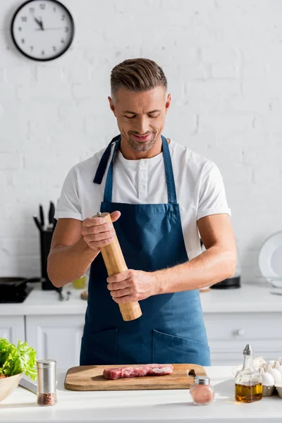 Bonito homem sorridente tempero bife antes de cozinhar — Fotografia de Stock