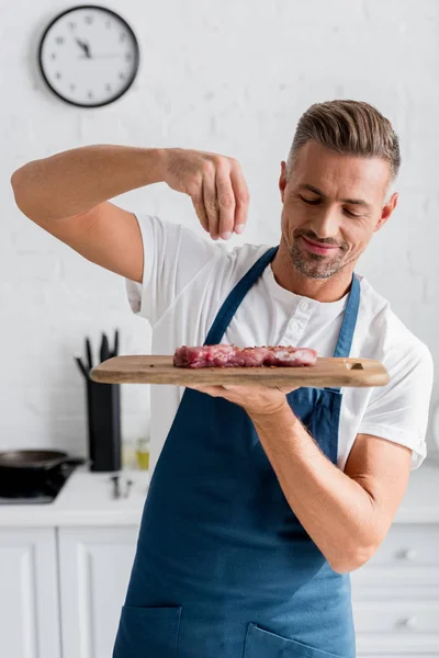 Älterer schöner Mann würzt Steak auf Holzbrett — Stockfoto