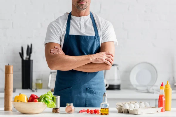 Uomo in grembiule in piedi su cucina con braccia incrociate — Foto stock