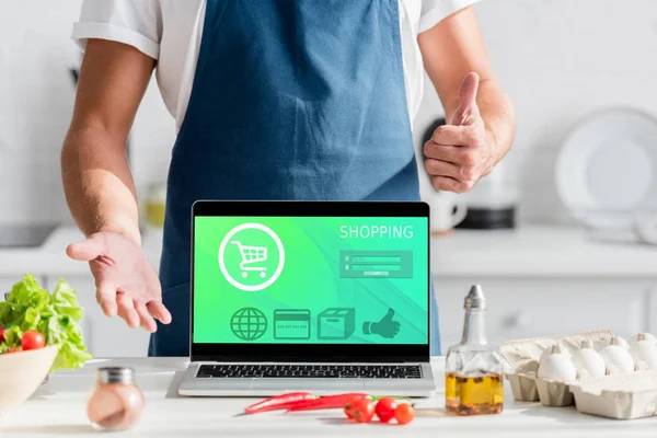 Vista recortada del hombre con el ordenador portátil que muestra pulgares hacia arriba en la cocina - foto de stock