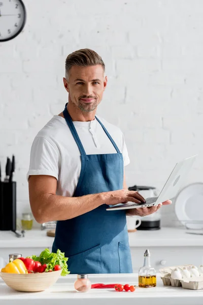 Uomo adulto con computer portatile in mano in piedi in cucina — Foto stock