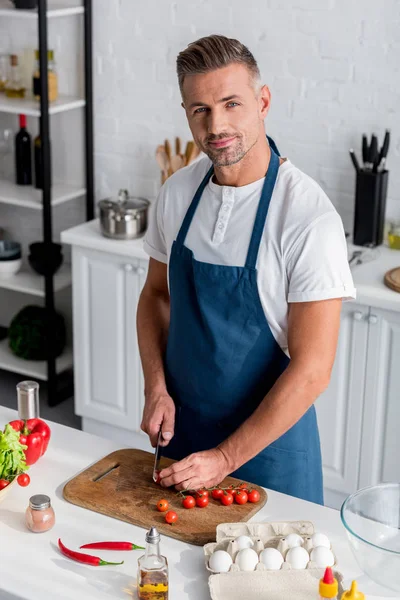 Homem adulto cortando tomates cereja na placa de corte na cozinha — Fotografia de Stock