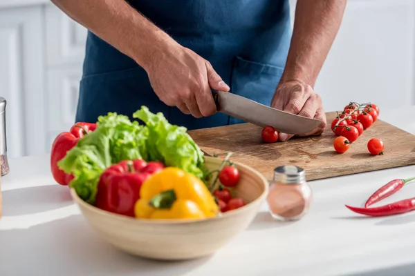 Teilansicht eines Mannes, der Kirschtomaten auf Schneidebrett in der Küche schneidet — Stockfoto