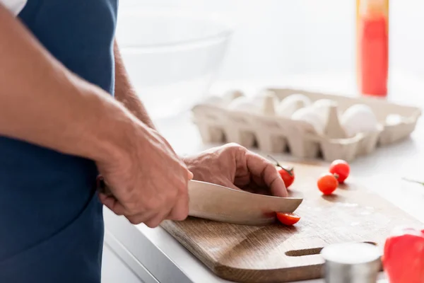 Partial view of man cutting with knife cherry tomatoes on cutting board — Stock Photo