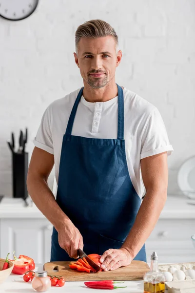 Bel homme coupant poivron sur planche à découper à la cuisine — Photo de stock