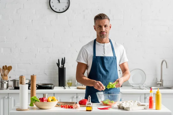 Erwachsener Mann in Schürze bereitet in Küche Salat zu — Stockfoto