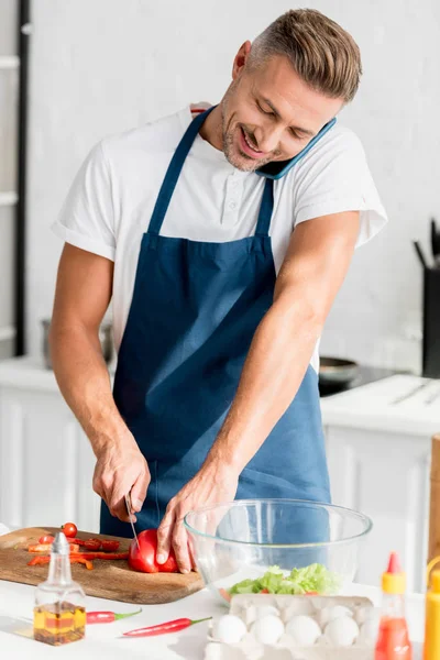 Mann spricht auf Smartphone, während er Paprika in der Küche schneidet — Stockfoto