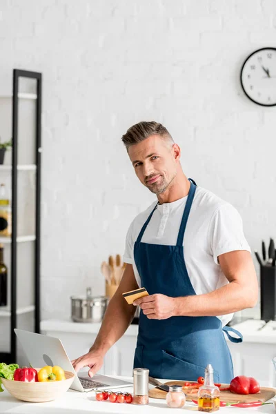 Homem adulto fazendo compras on-line no laptop na cozinha — Fotografia de Stock