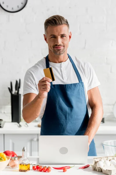 Hombre guapo haciendo compras en línea en el ordenador portátil en la cocina - foto de stock