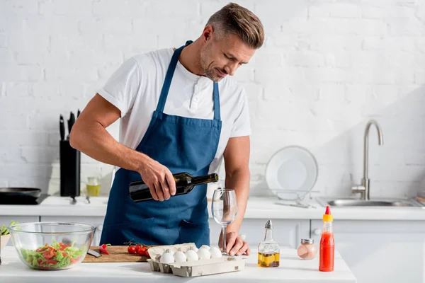 Bell'uomo che versa il vino nel bicchiere in cucina — Foto stock