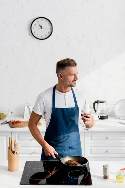 Hombre en delantal con copa de filete de cocina de vino en la sartén - foto de stock