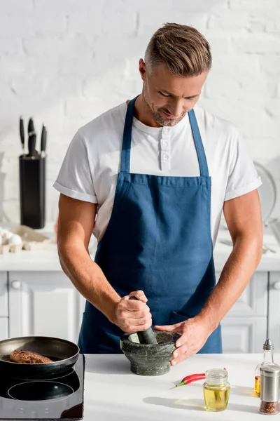 Uomo adulto schiacciamento spezie sul tavolo della cucina — Foto stock