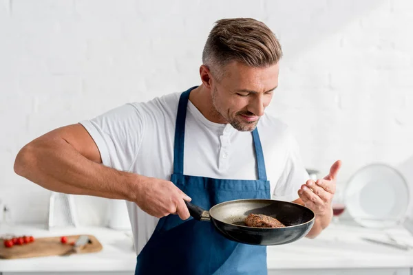 Handsome man in apron smelling cooked steak — Stock Photo