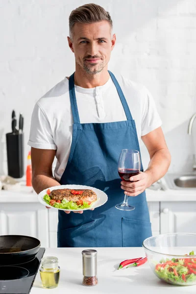 Bel homme avec viande cuite dans une main et verre de vin dans l'autre — Photo de stock