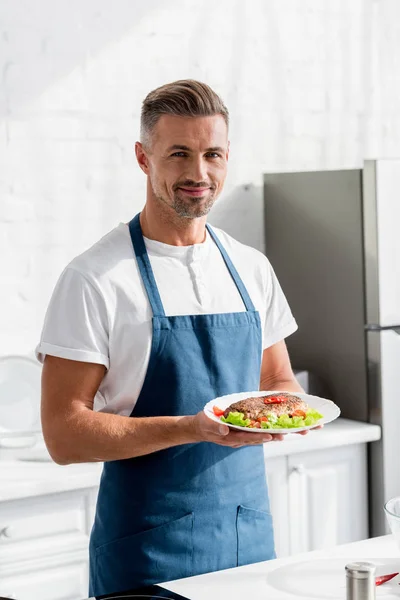 Uomo in grembiule con bistecca cotta in cucina — Foto stock