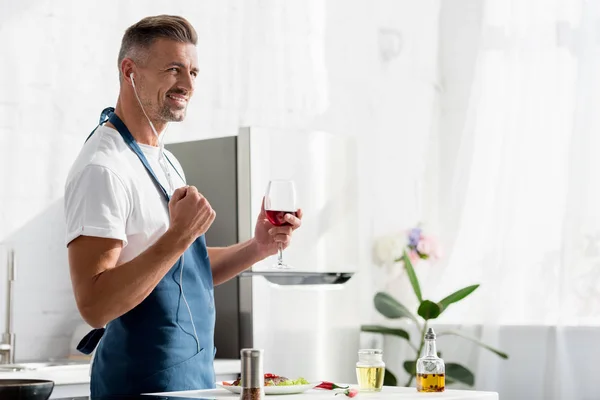 Homem sorridente com copo de vinho ouvindo música na cozinha — Fotografia de Stock