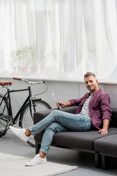 Uomo sorridente seduto sul divano con tablet digitale — Foto stock