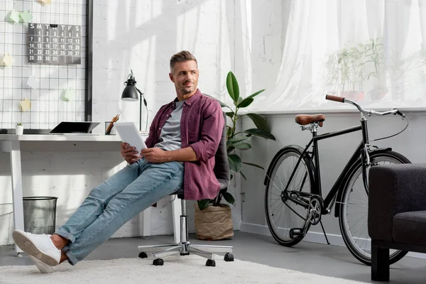 Улыбающийся мужчина сидит на стуле с цифровым планшетом в руках — стоковое фото