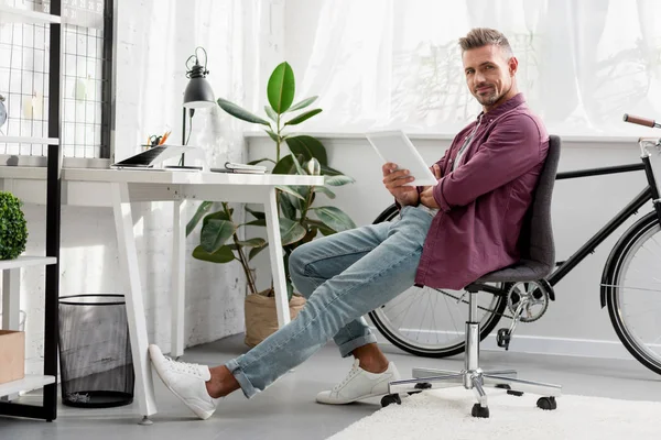 Расслабляющий мужчина сидит на стуле с цифровым планшетом в домашнем офисе — стоковое фото