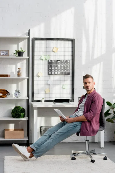 Homem adulto sentado na cadeira com tablet digital em casa escritório — Fotografia de Stock
