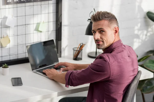 Homme assis à table avec ordinateur portable et smartphone au bureau à la maison — Photo de stock