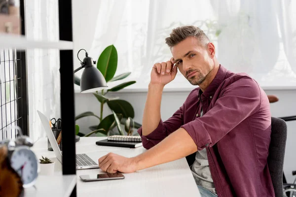 Чоловік сидить за столом з ноутбуком і смартфоном в домашньому офісі — стокове фото