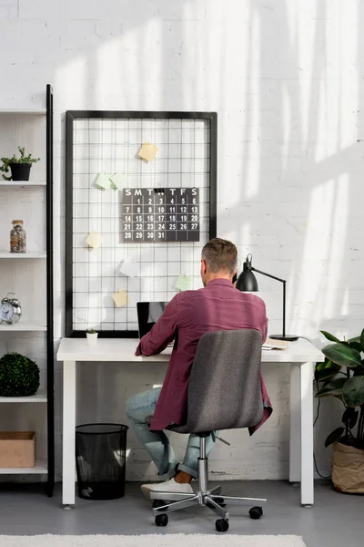 Vista traseira do homem sentado no local de trabalho no escritório de casa — Fotografia de Stock