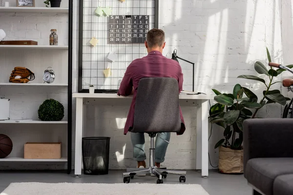 Rückansicht eines Mannes, der auf einem Stuhl sitzt und zu Hause im Büro arbeitet — Stockfoto