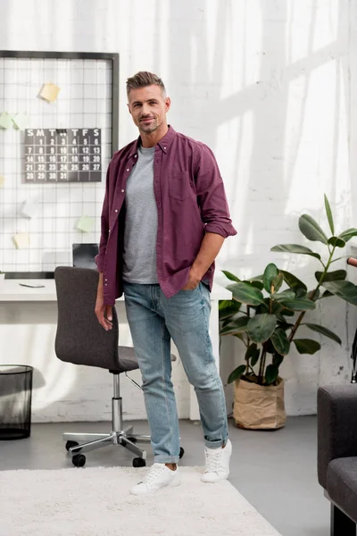 Handsome man standing near workplace with hand in pocket — Stock Photo