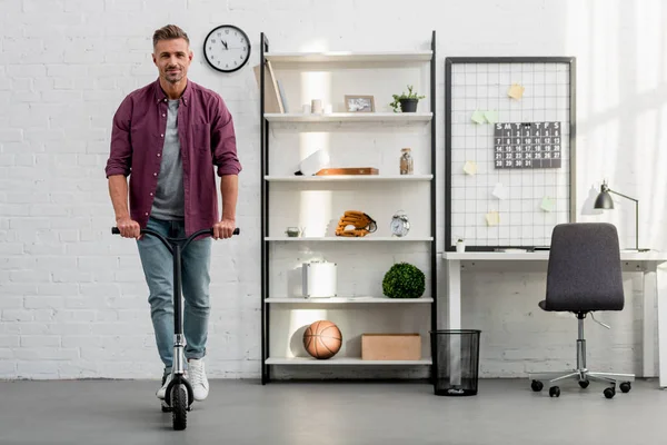 Homem bonito montando scooter em casa escritório — Fotografia de Stock