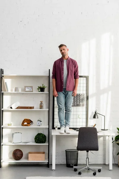 Людина з втомленим обличчям, що стоїть на столі в домашньому офісі — стокове фото