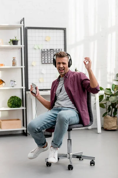 Homme écoutant de la musique et chantant fort assis sur la chaise au bureau à la maison — Photo de stock