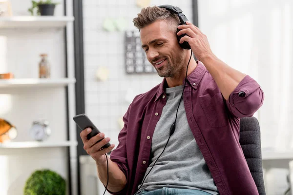 Hombre feliz escuchando música mientras está sentado en la silla en la oficina en casa - foto de stock