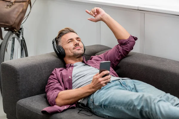 Glücklicher Mann, der Musik hört und singt, während er auf dem Sofa liegt — Stockfoto