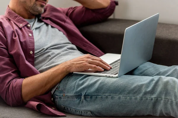 Close-up de homem deitado no sofá e trabalhando no laptop no escritório em casa — Fotografia de Stock