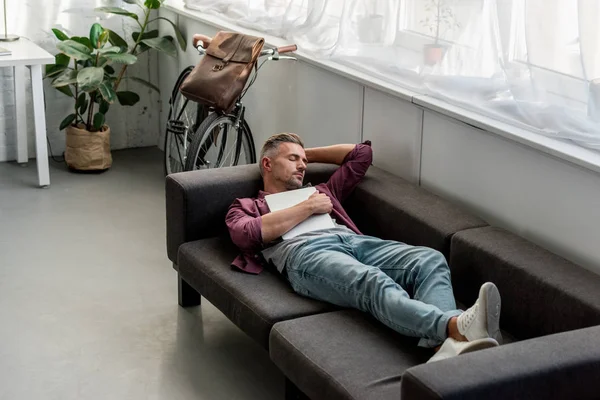 Müder Mann liegt mit Laptop auf Sofa und schläft zu Hause im Büro — Stockfoto