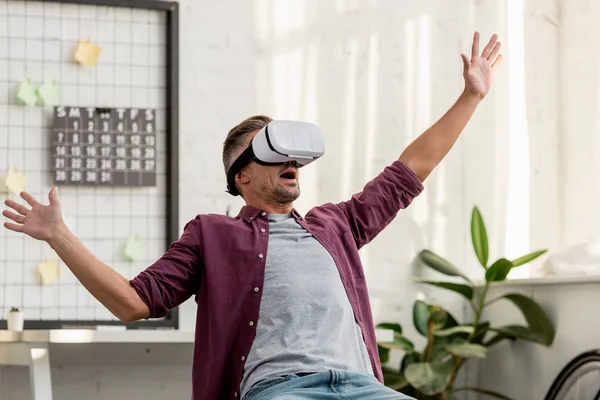 Hombre asustado sentado en la silla en auriculares de realidad virtual - foto de stock