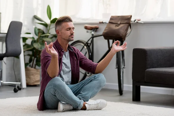 Hombre concentrado sentado en el suelo practicando yoga en casa oficina - foto de stock