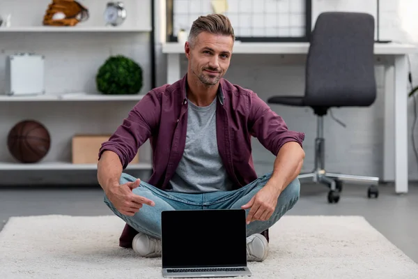 Красивый мужчина сидит в домашнем офисе с ноутбуком и указывает на чистый экран — стоковое фото
