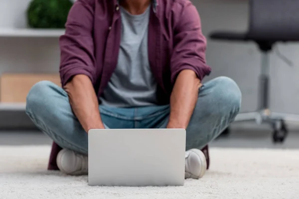 Cropped view of man sitting on carpet and working on laptop — Stock Photo
