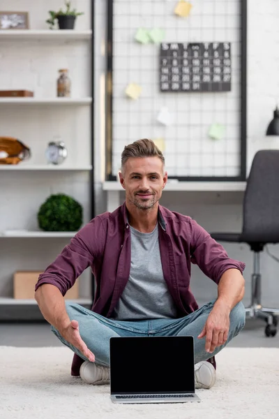 Handsome man sitting in home office with laptop and pointing at blank screen — Stock Photo