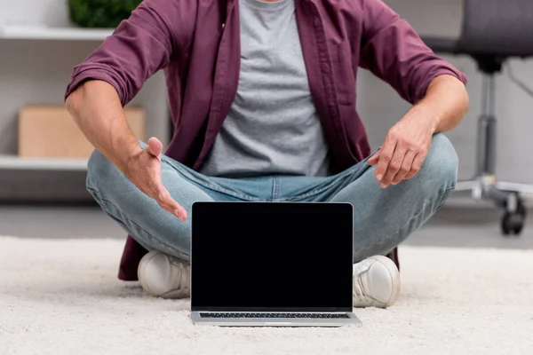 Cropped view of man sitting with laptop on carpet — Stock Photo