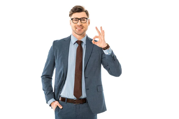 Homme d'affaires souriant en lunettes et costume montrant ok signe isolé sur blanc — Photo de stock