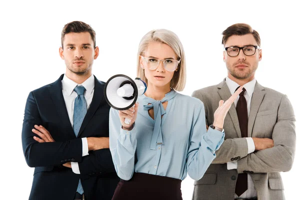 Dissatisfied businesswoman holding megaphone while colleagues standing with arms crossed isolated on white — Stock Photo