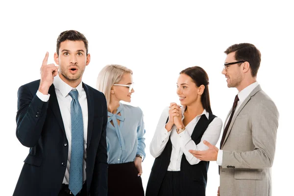 Sorprendido empresario teniendo idea y apuntando hacia arriba mientras compañeros de trabajo lluvia de ideas detrás aislado en blanco - foto de stock